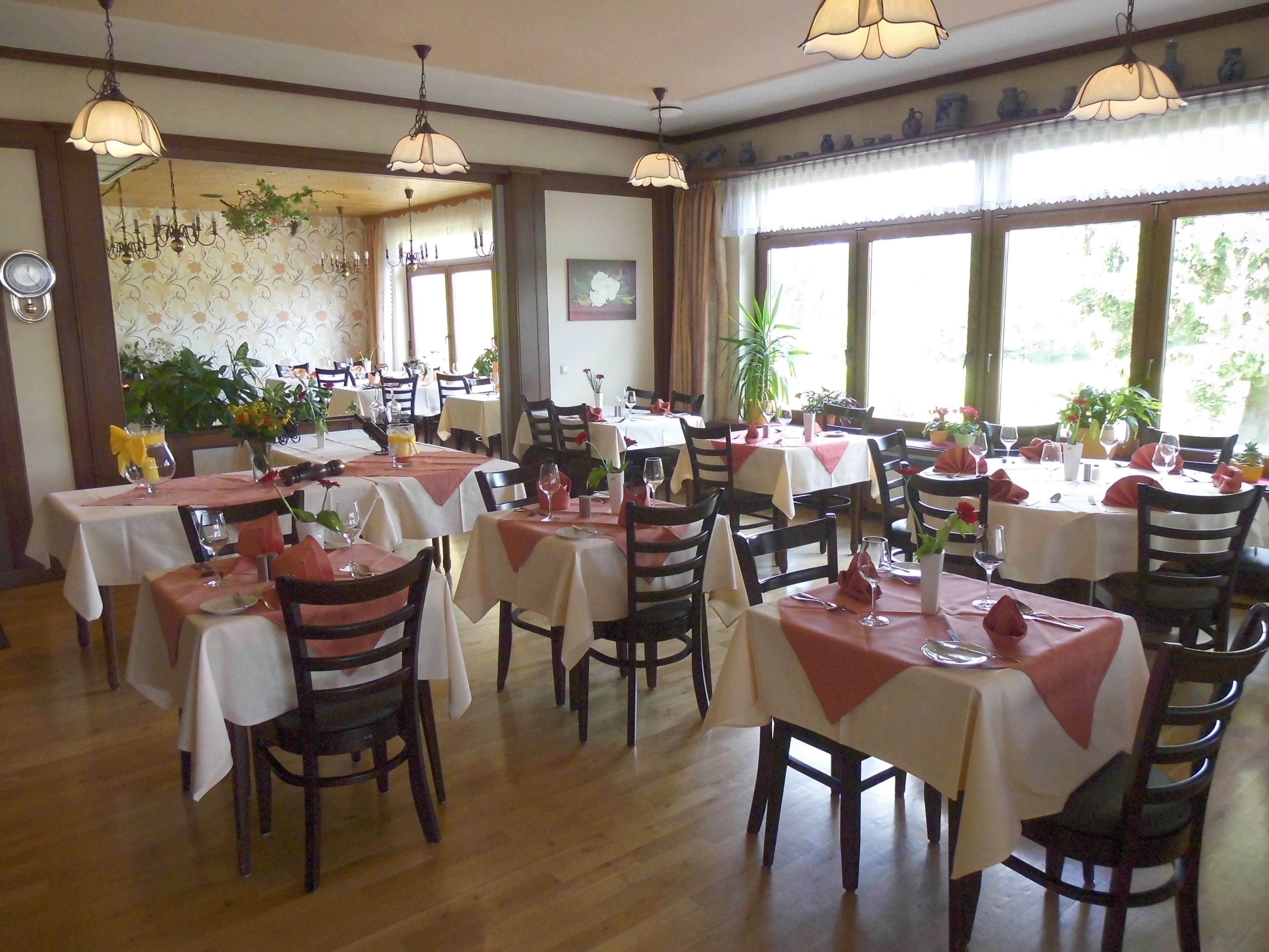 Ein Restaurant mit mehreren Tischen, jeder Tisch mit weißer Tischdecke und roten Servietten.