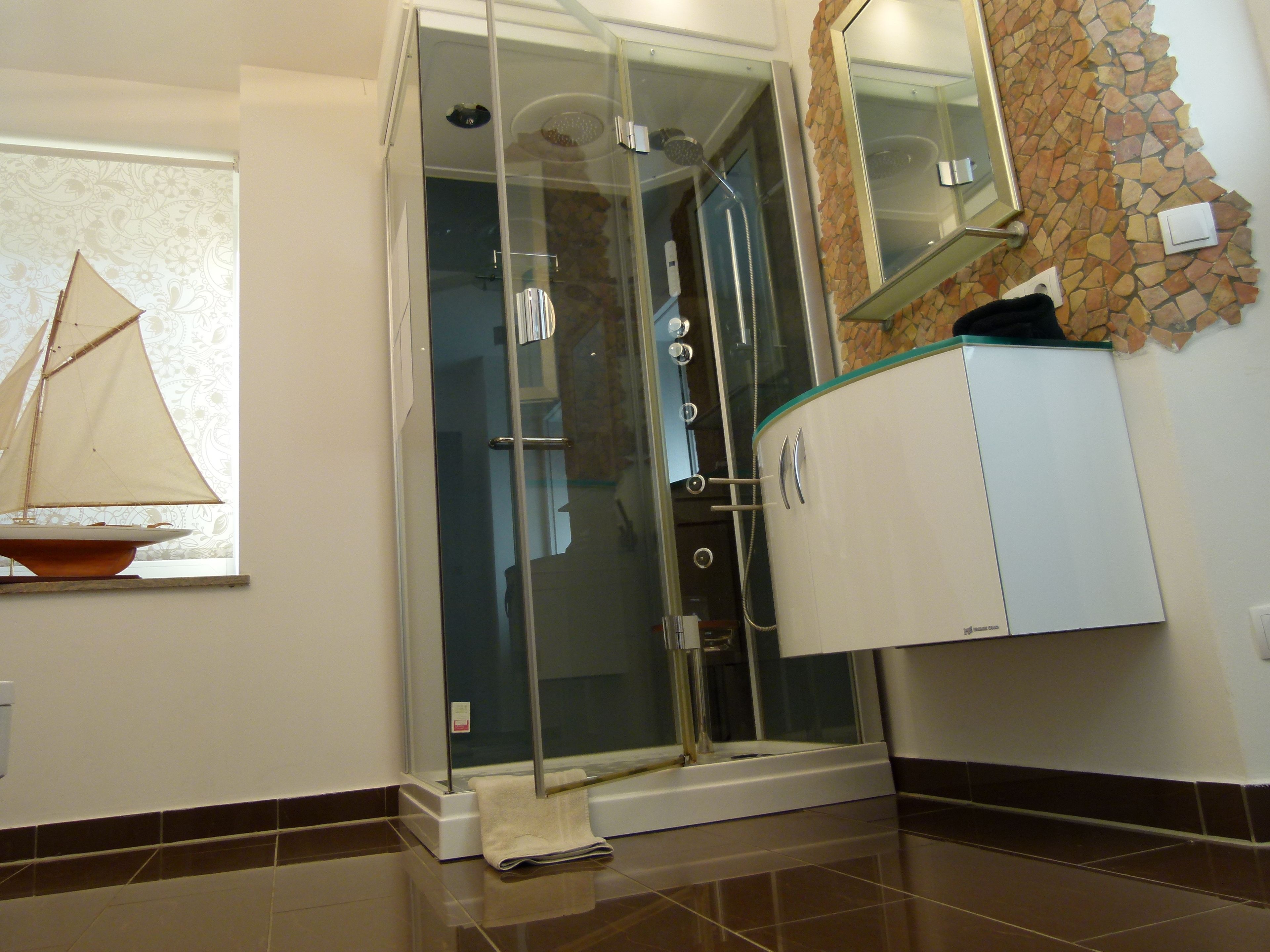 A bathroom with a glass-enclosed shower, a white cabinet, and a decorative sailboat model on a shelf.