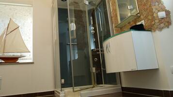 A bathroom with a glass-enclosed shower, a white cabinet, and a decorative sailboat model on a shelf.