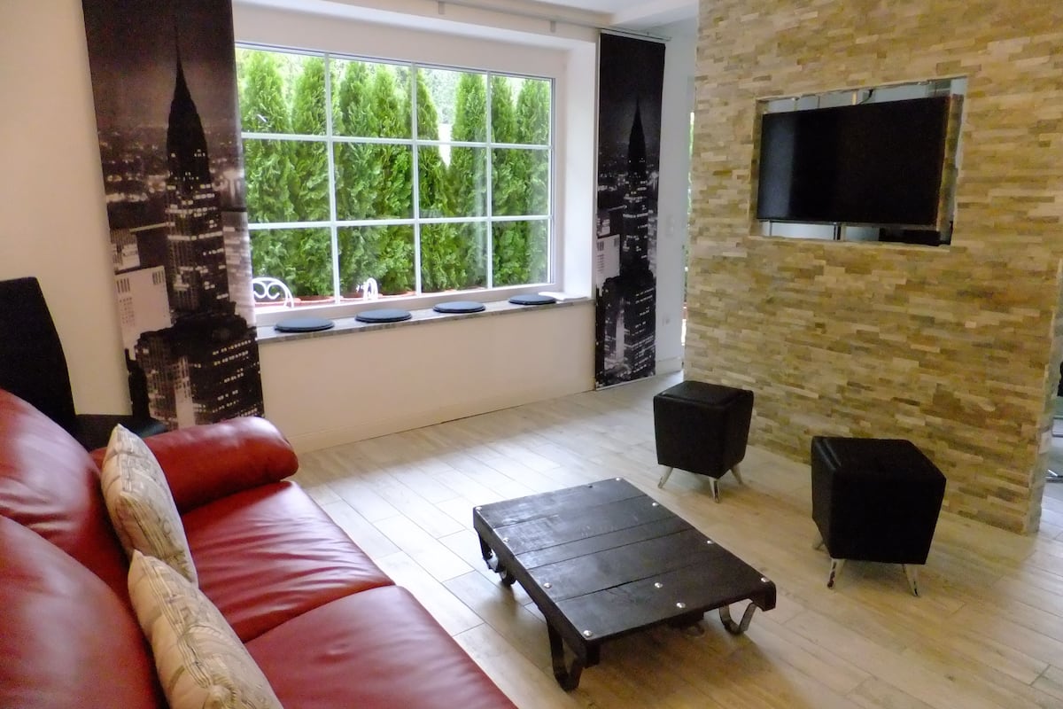 A living room with a red sofa, a black coffee table, and a TV mounted on a stone wall.