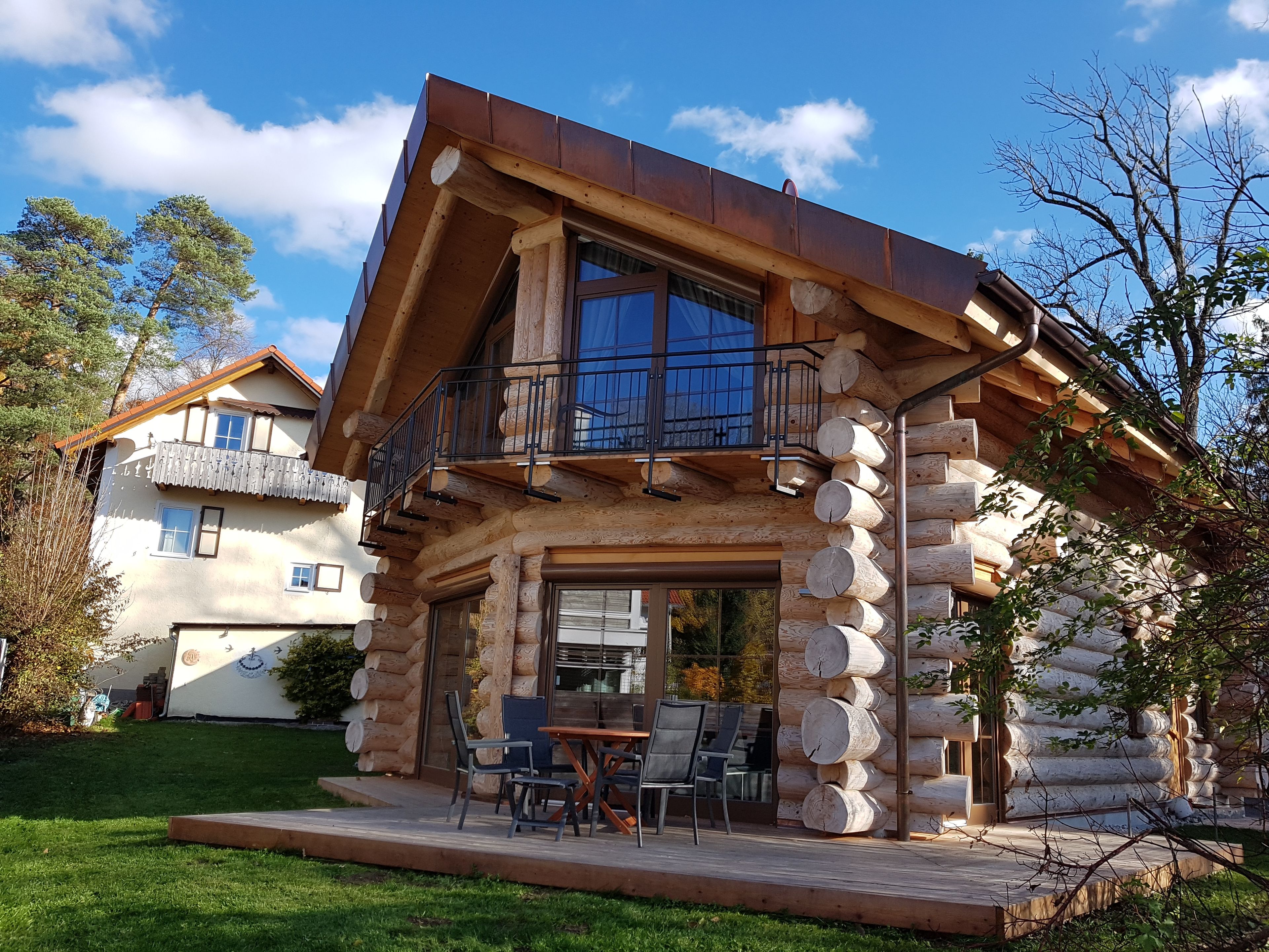 Una cabaña de troncos con balcón y un patio con mobiliario exterior.