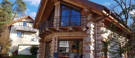 Una cabaña de troncos con balcón y un patio con mobiliario exterior.