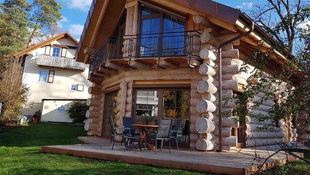 A log cabin with a balcony and a patio area with outdoor seating.