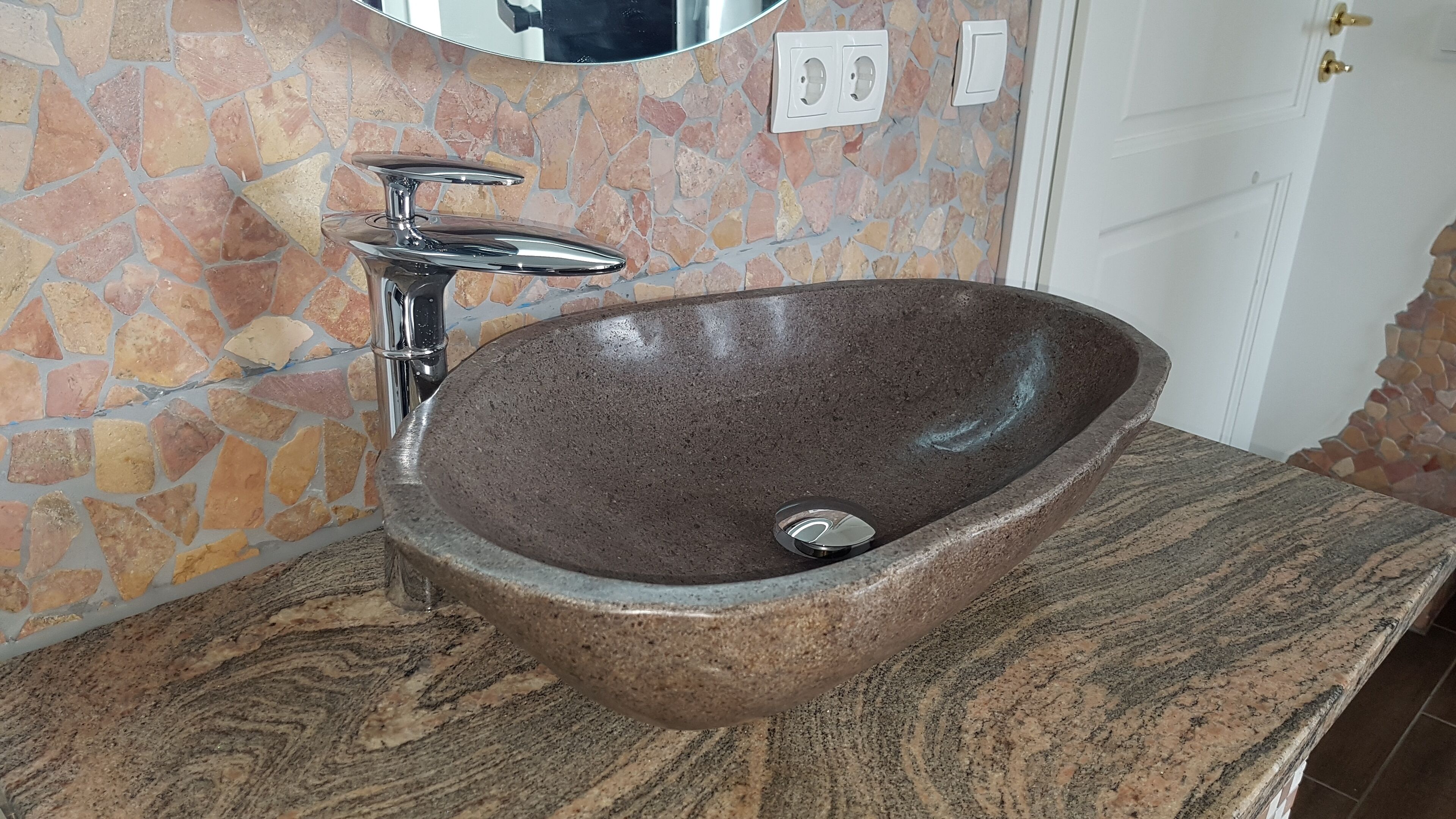 A bathroom with a stone sink, a mirror, and a door.