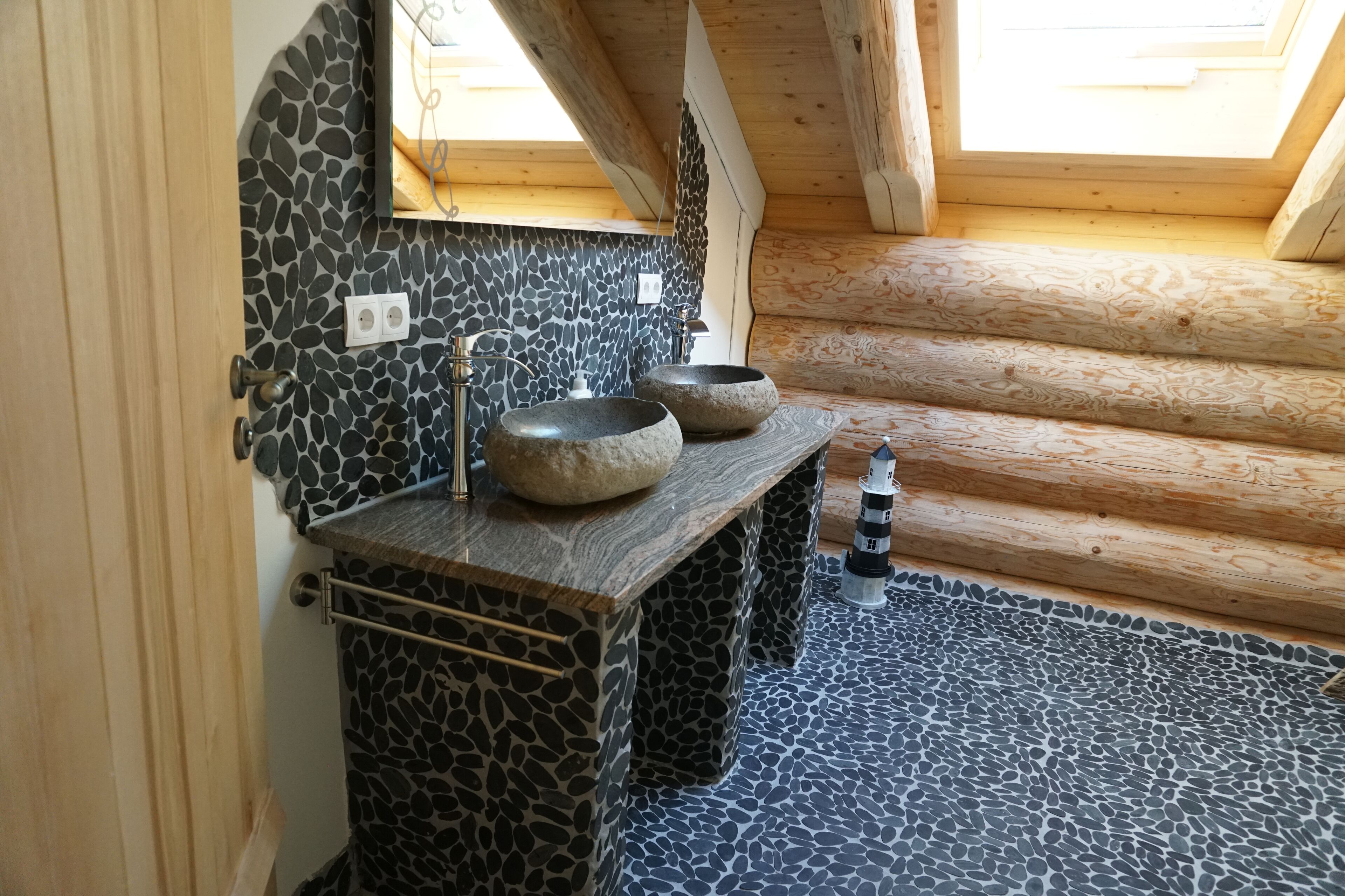 A bathroom with a stone mosaic floor, two stone sinks, a wooden vanity, and a skylight.