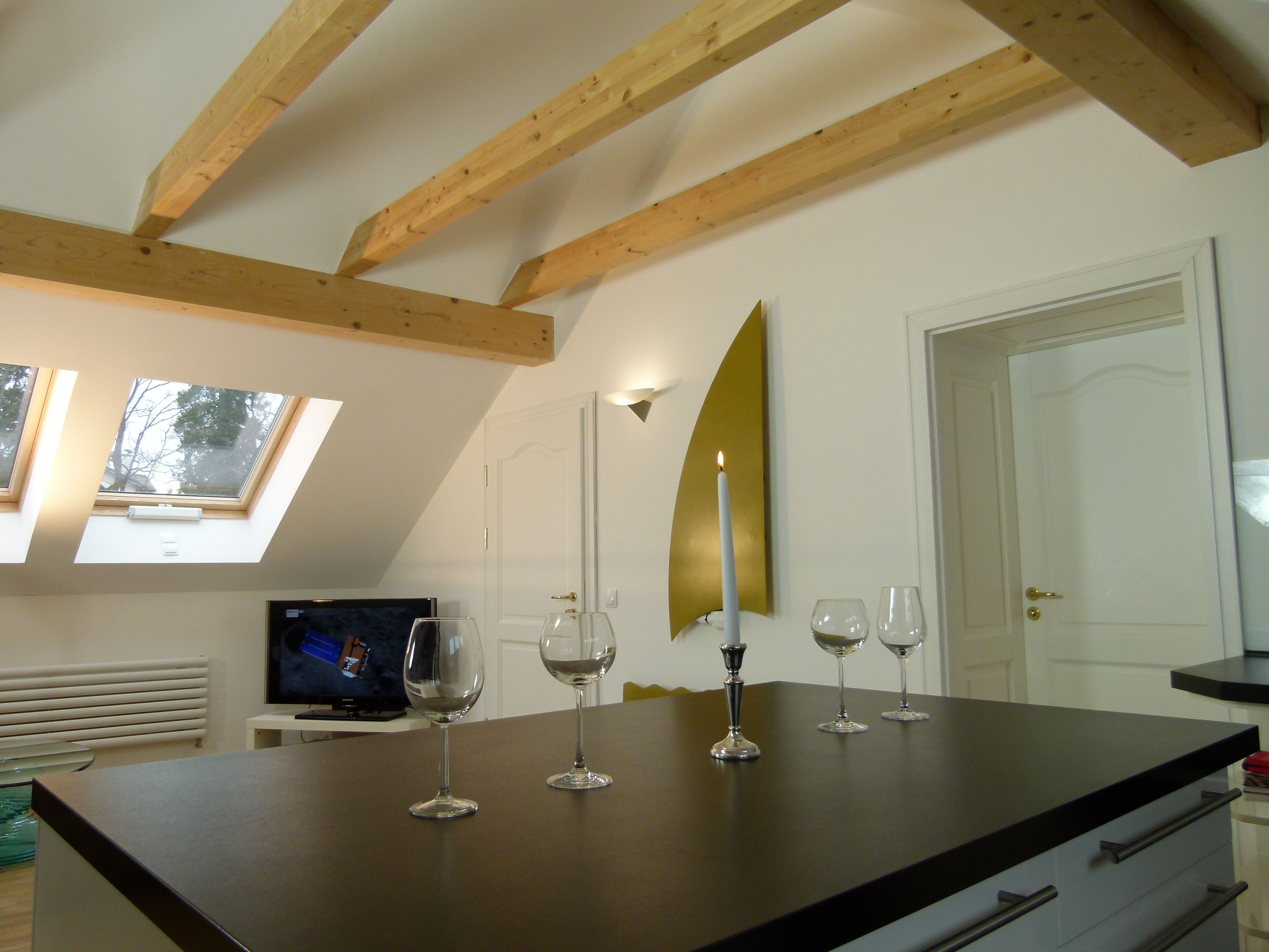 A modern kitchen with a dark countertop, wooden beams, a skylight, and a TV in the background.