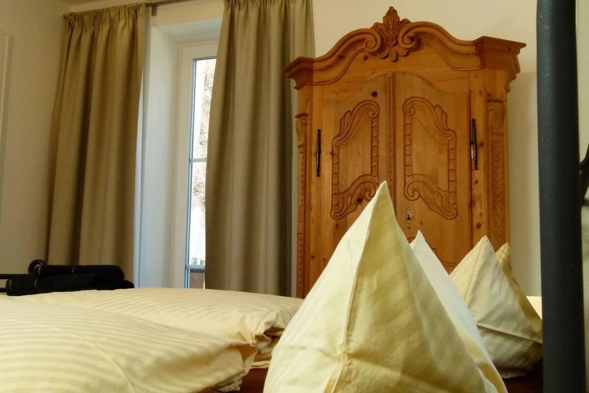 A bedroom with two beds, a wooden wardrobe, and a window with curtains.
