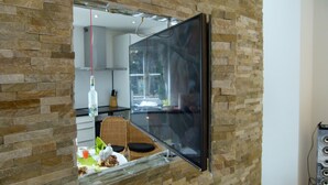 A modern kitchen with a stone wall, a flat-screen TV, and a dining area with a table set for two.