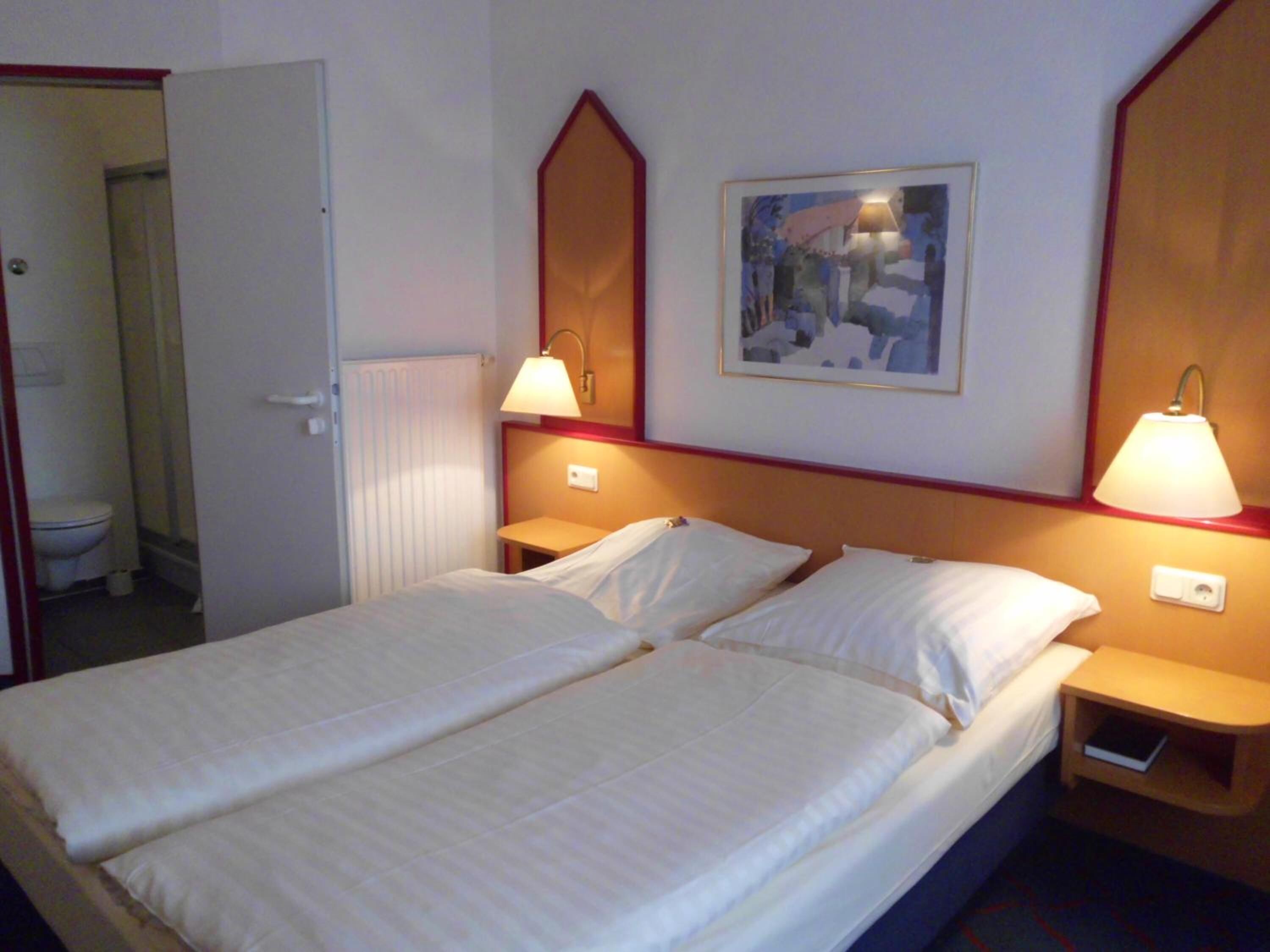 A hotel room with two beds, a painting on the wall, and two bedside lamps.