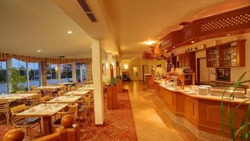 A hotel restaurant with a buffet bar, dining tables, and chairs.