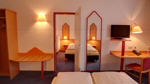 Ein Hotelzimmer mit zwei Betten, einem Schreibtisch mit Fernseher, einem Spiegel und einem Kleiderschrank.