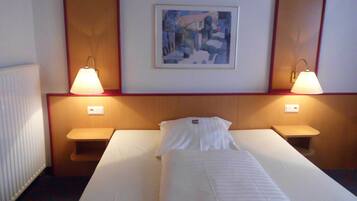 Een hotelkamer met een enkel bed, twee bedlampen, een ingelijst schilderij aan de muur en een radiator.