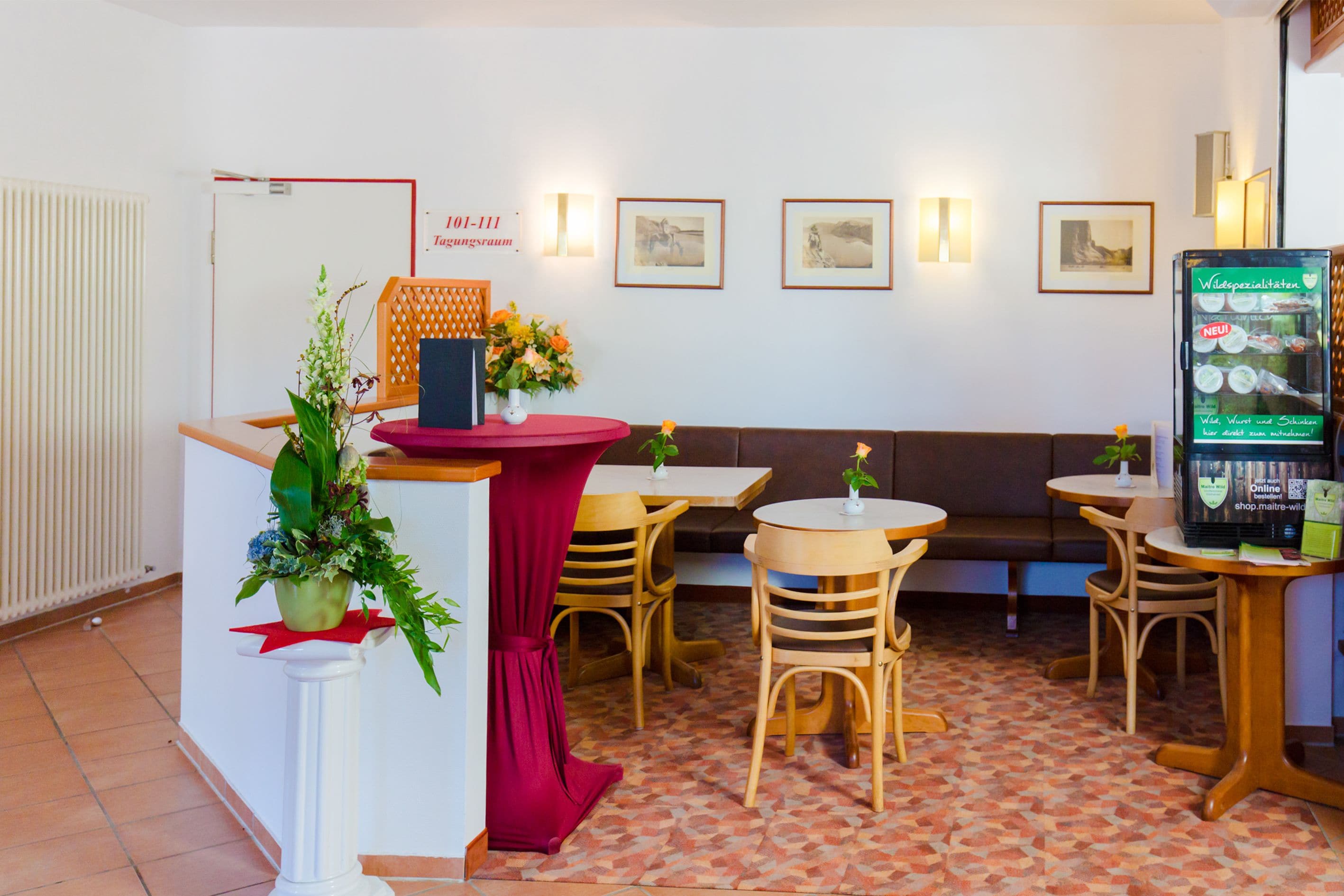 Un hall de hotel con mostrador de recepción, zona de estar y un refrigerador exhibiendo un menú.