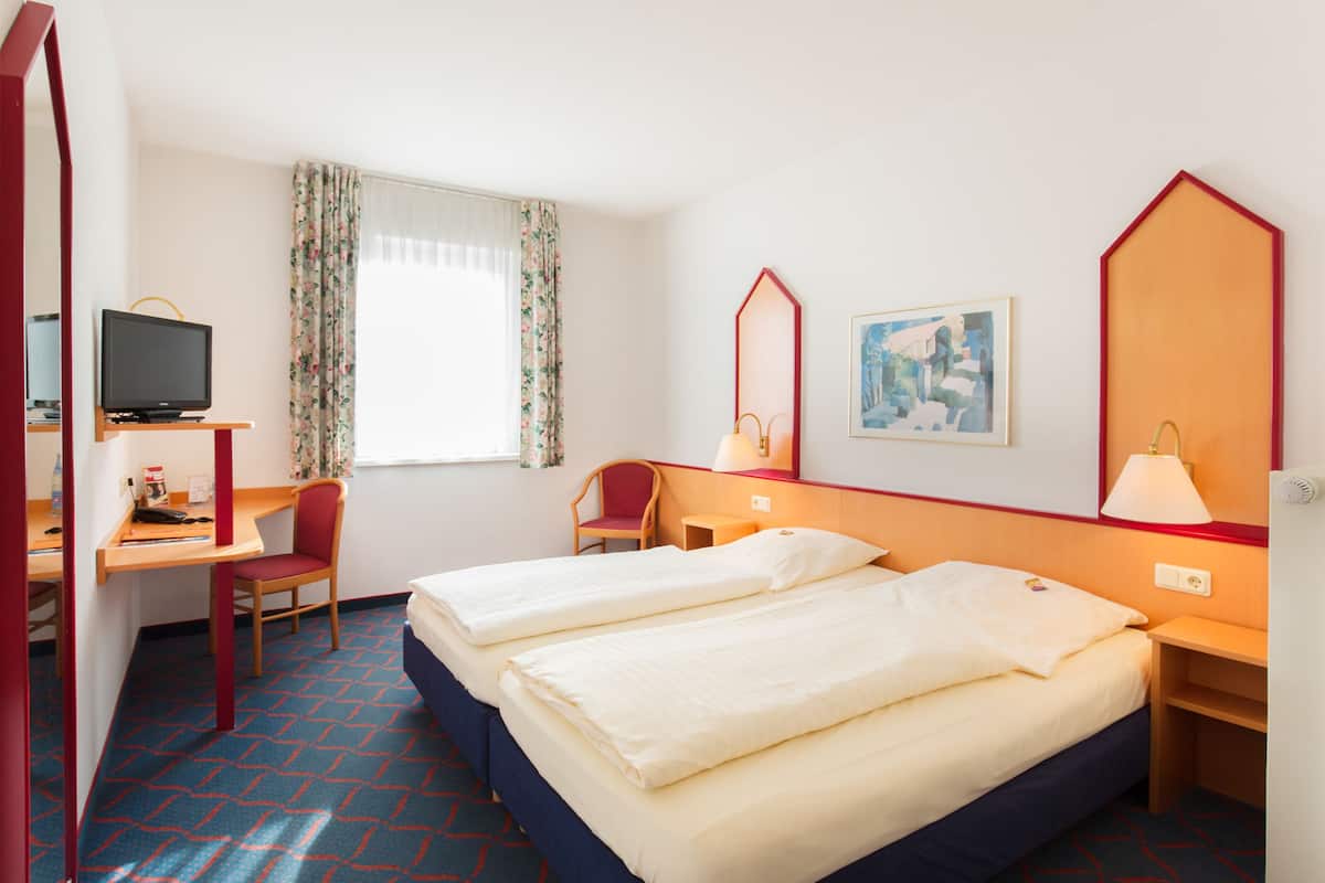 Une chambre d’hôtel avec deux lits, un bureau avec une chaise, une télévision et une fenêtre avec des rideaux.