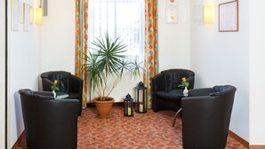 Ein Zimmer mit zwei schwarzen Sesseln, einem Blumentopf, einem kleinen Tisch und einem Fenster mit Vorhängen.