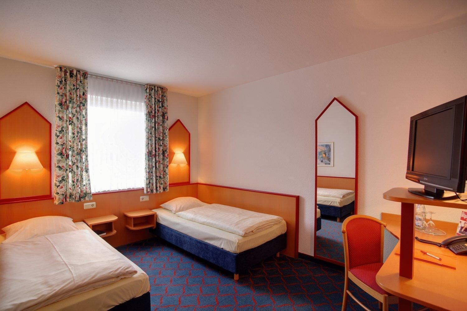 A hotel room with two beds, a desk with a chair, a TV, and a mirror.