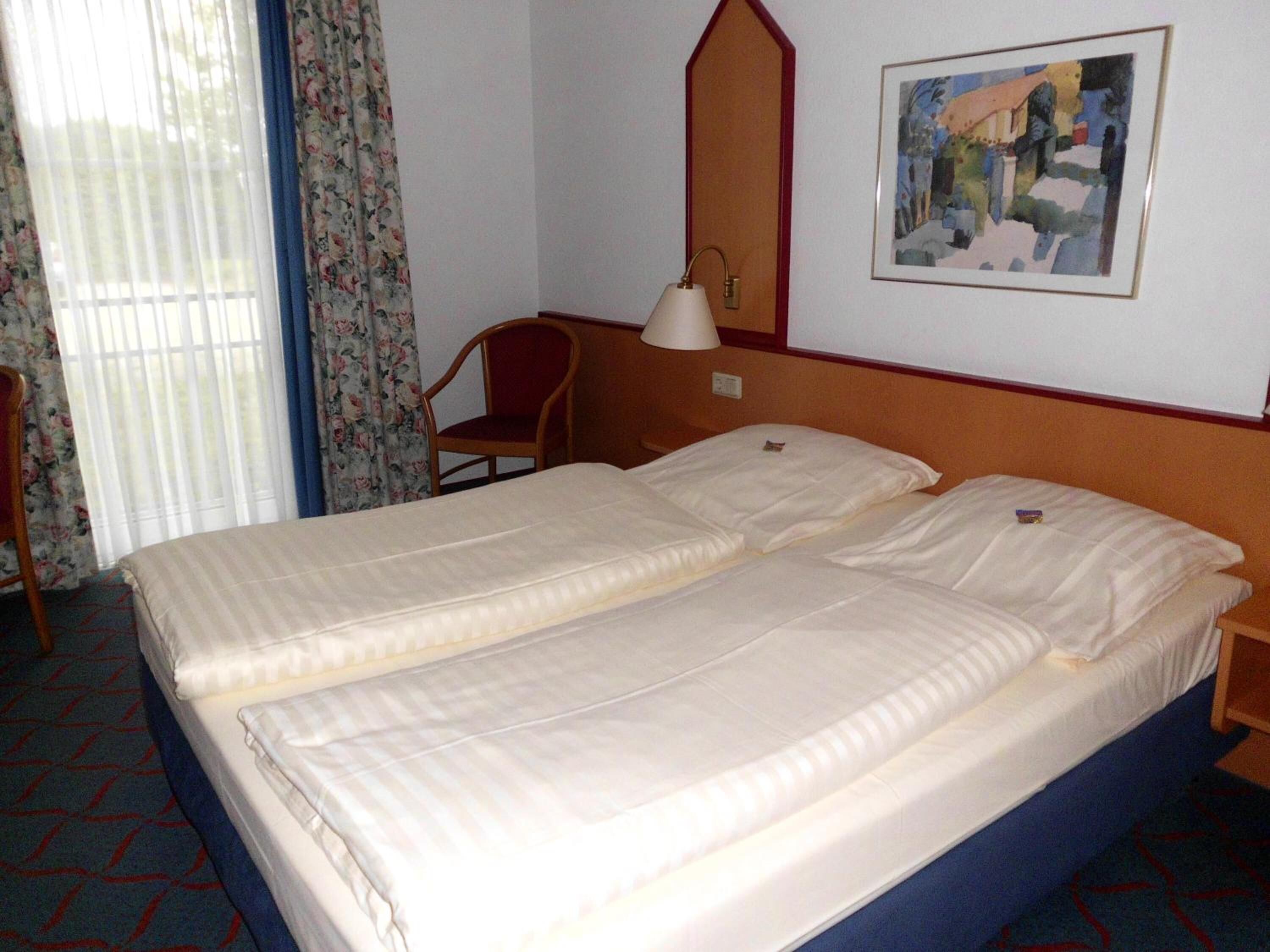 A hotel room with a double bed, a chair, a bedside table, a lamp, and a painting on the wall.