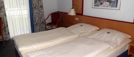A hotel room with a double bed, a chair, a bedside table, a lamp, and a painting on the wall.