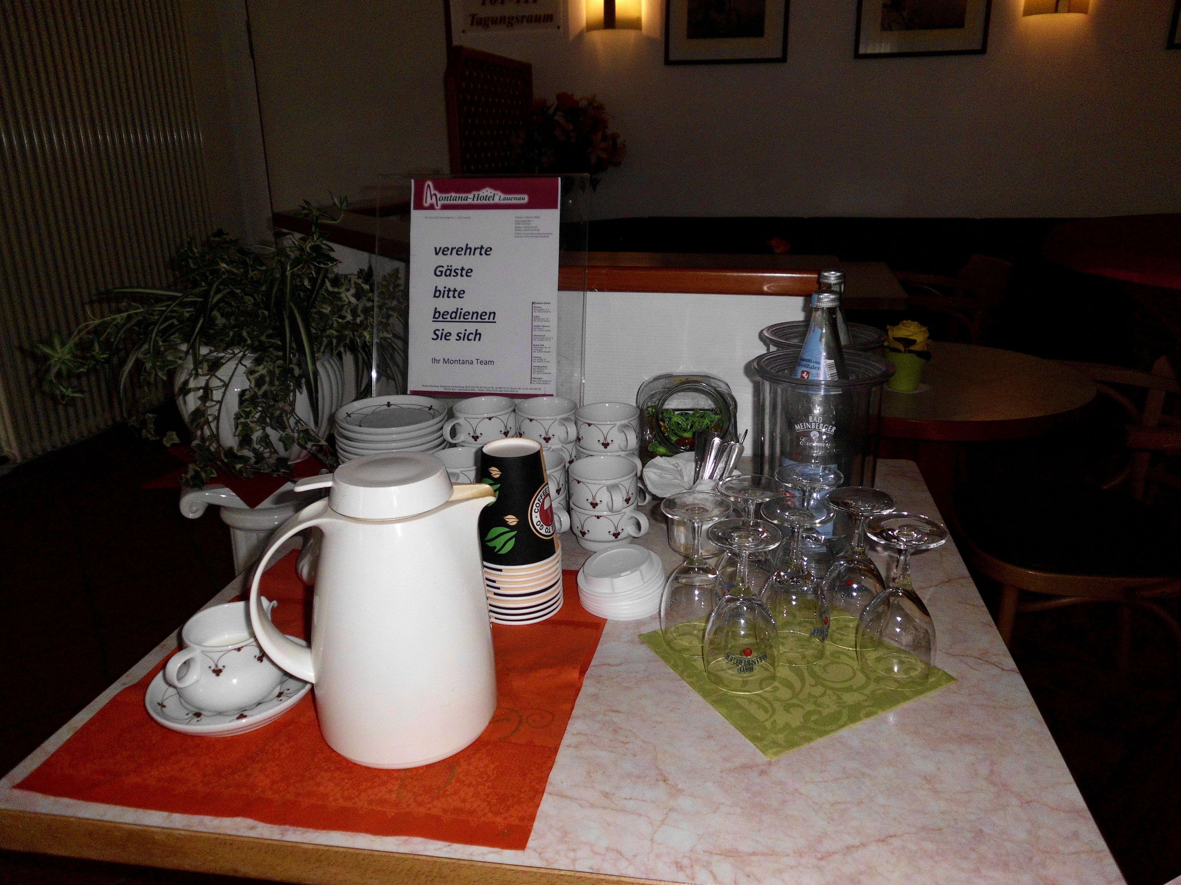 Une table dressée avec des théières, des tasses et des verres à vin blancs, et un panneau indiquant un supplément de service.