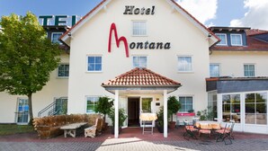 Ein Hotel namens "Montana" mit überdachter Eingangspartie, Außenbereich zum Sitzen und einer gepflasterten Terrasse.