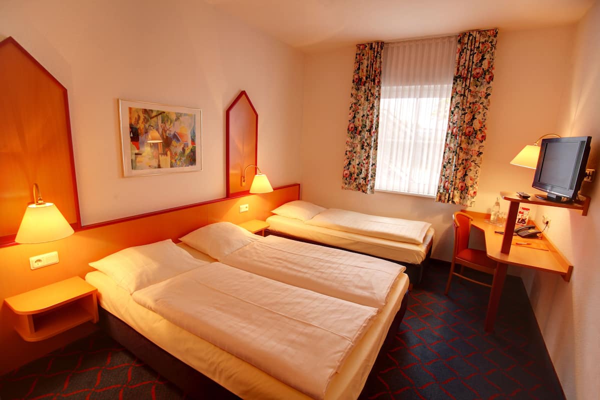 Une chambre d’hôtel avec deux lits, un bureau avec une chaise, une télévision et une fenêtre avec des rideaux.