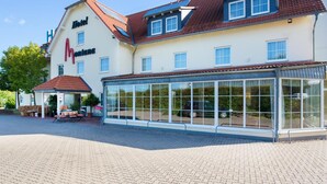 Ein Hotel mit großer Glasfassade, rotem Ziegeldach und einer überdachten Außenbereich-Sitzgelegenheit.