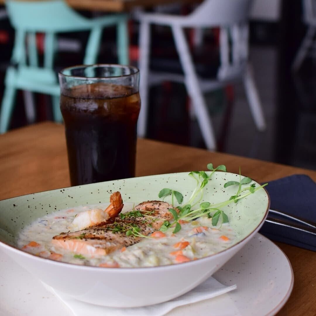 A bowl of creamy soup with shrimp and vegetables, served on a white plate with a green rim.