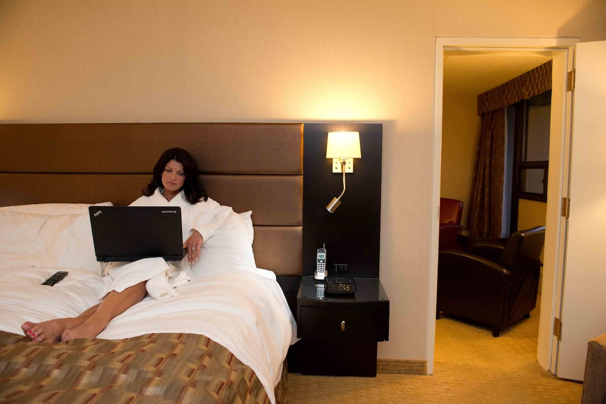 A hotel room with a bed, a nightstand with a lamp, a chair, and a door.