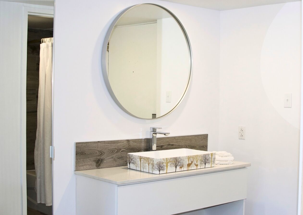 A bathroom with a white vanity, a round mirror, and a sink with a decorative backsplash.