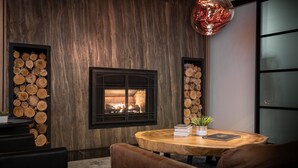 A cozy room with a fireplace, wooden logs on the walls, a round wooden table, and a brown leather sofa.