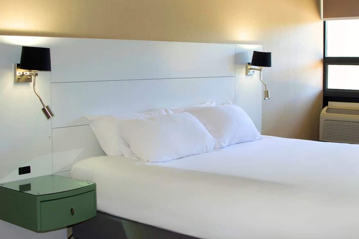 A hotel room with a large bed, two bedside tables, and wall-mounted lamps.