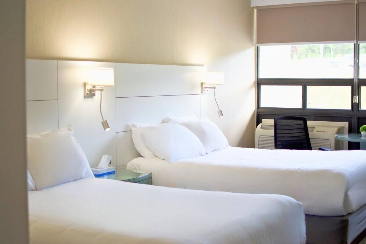 A hotel room with two beds, a desk, a chair, and a window with blinds.