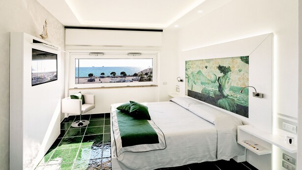 Une chambre à coucher moderne avec un lit, un banc, une fenêtre donnant sur la mer et un tableau accroché au mur.