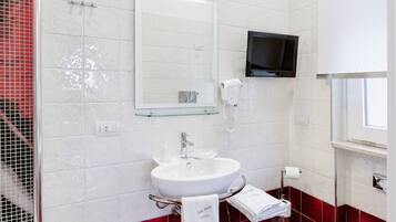 Une salle de bain avec un lavabo blanc, un miroir, un téléviseur fixé au-dessus du lavabo et un espace douche dont les murs sont recouverts de carreaux rouges.