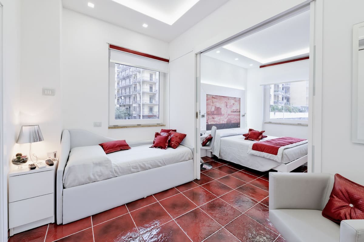 A modern bedroom with two beds, a nightstand, a lamp, and a large mirror.