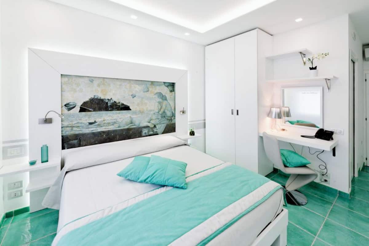 A modern bedroom with a large bed, a desk, and a wall-mounted TV.