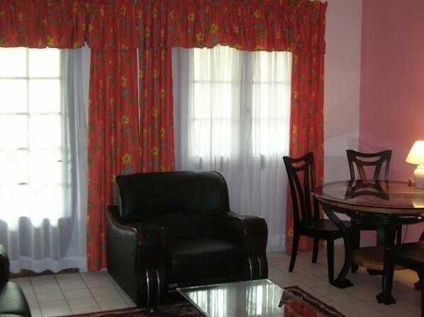 A living room with a black armchair, a glass coffee table, a dining table with chairs, and a lamp. - Résidence Saint-Jacques Bord de Mer (Pointe-Noire)