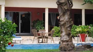 A pool area with a table and chairs, surrounded by potted plants and a palm tree. - Résidence Saint-Jacques Bord de Mer (Pointe-Noire)