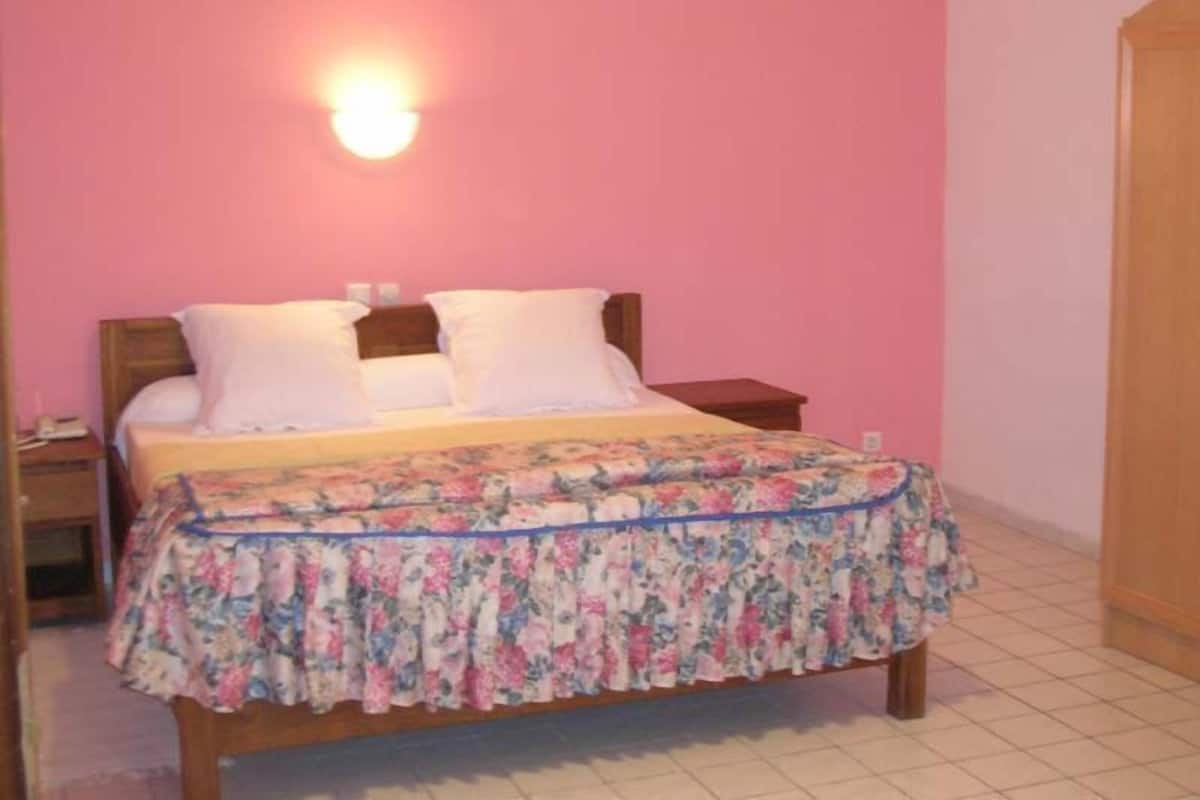 Quarto com cama, mesa de cabeceira, luminária na parede e guarda-roupa de madeira.