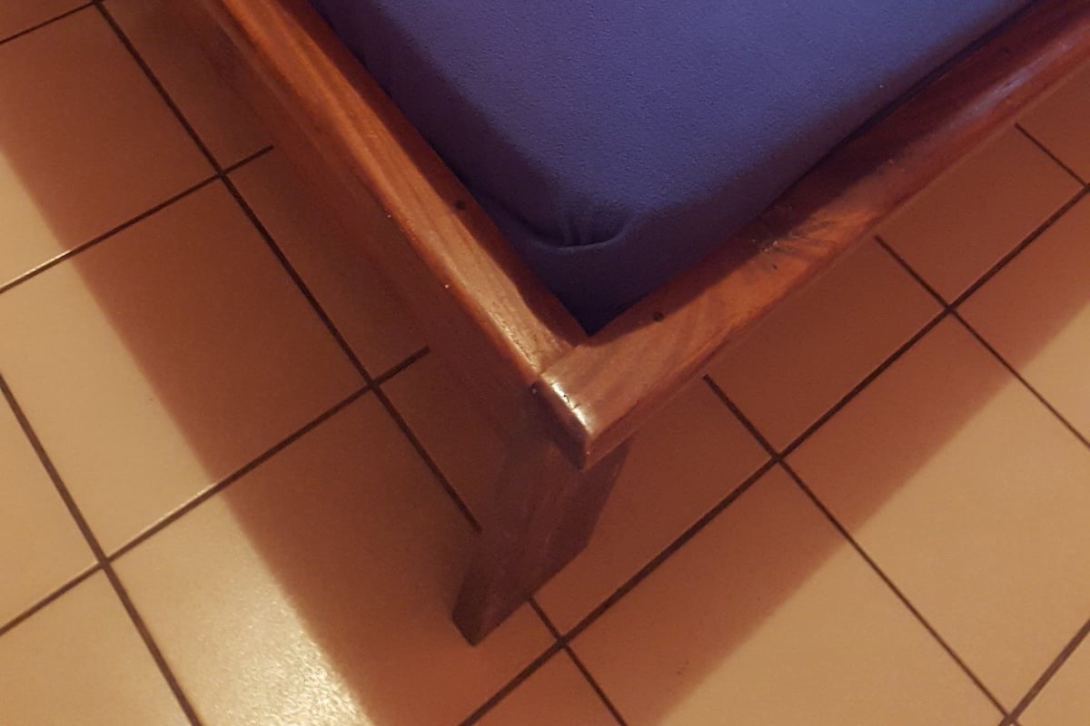Uma cama com colcha azul, almofadas brancas e cabeceira de madeira.