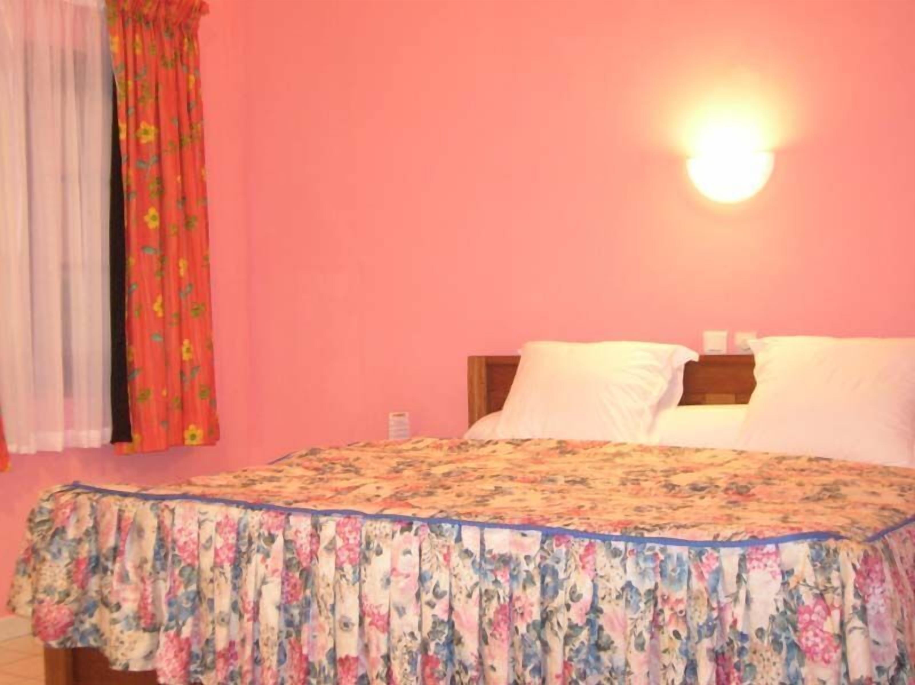 Un dormitorio con cubrecama floral, cabecera de madera y lámpara de pared.