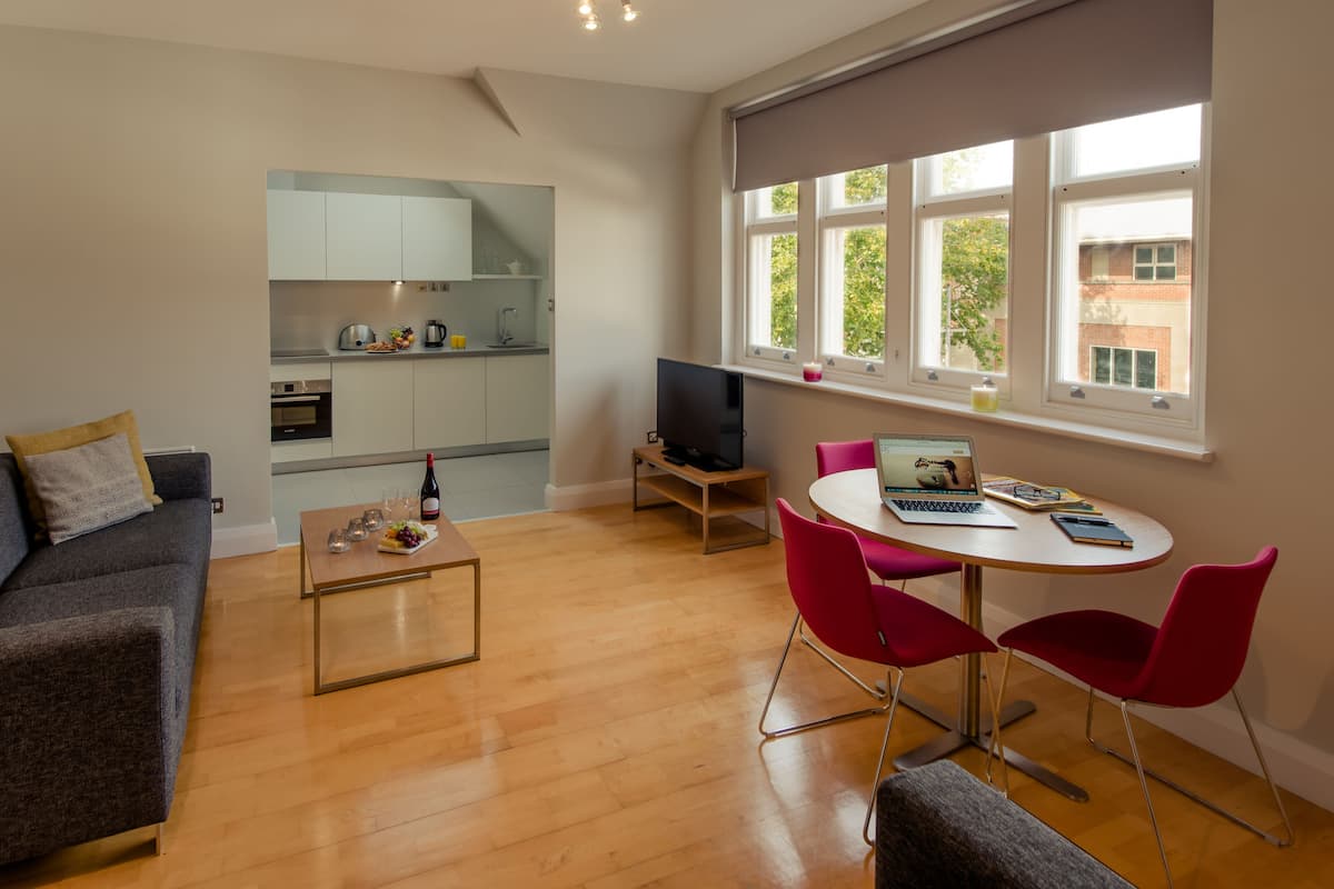 A modern living room with a sofa, a coffee table, and a dining area with a table and chairs. A kitchen is visible in the background.