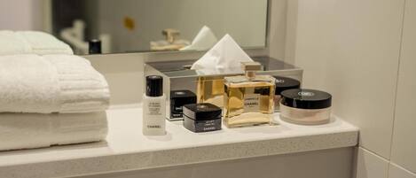 Un mueble de baño con artículos de aseo personal, incluyendo una botella de Chanel Le Blanc de Chanel, un frasco de perfume y un compacto de maquillaje.