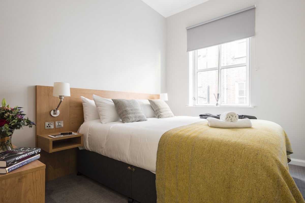 A neatly arranged bedroom with a bed, bedside table, lamp, and a window.