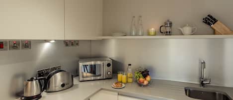A modern kitchen with a microwave, toaster, kettle, and sink. There are bottles, a teapot, and a knife block on the counter.