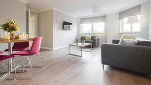 A modern living room with a grey sofa, a dining table with pink chairs, and a coffee table. - PREMIER SUITES Reading (Reading)