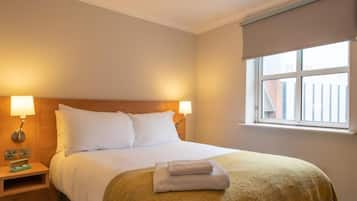A hotel room with a bed, bedside lamps, a window with a view, and a neatly made bed with a folded towel.