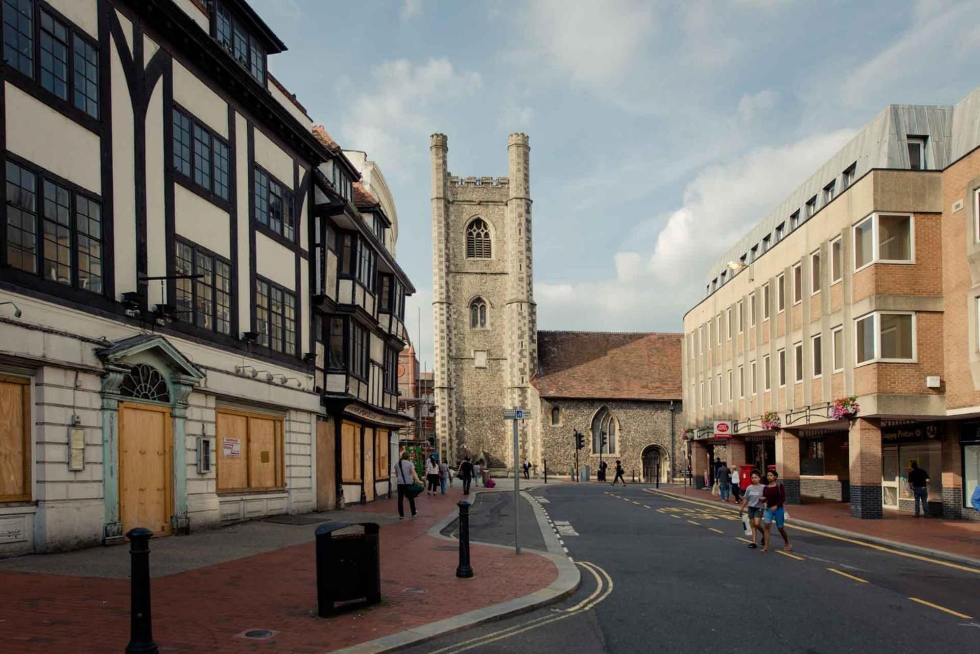A street with historic buildings, a church tower, and pedestrians.
