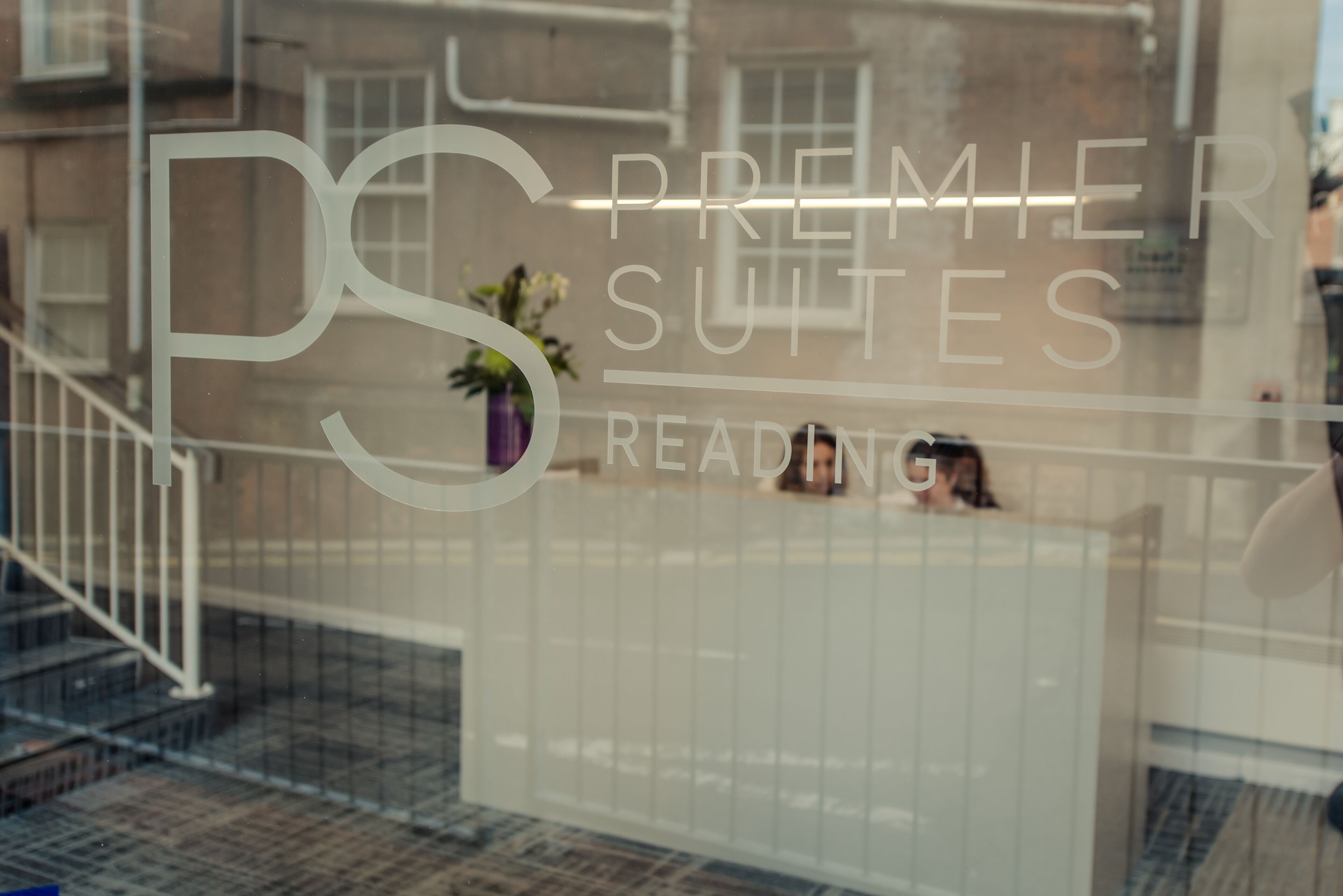 A glass window with the text "Premier Suites Reading" and a partial view of a staircase.