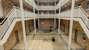 A spacious atrium with a central seating area, white railings, and a brick building facade. - PREMIER SUITES Reading (Reading)